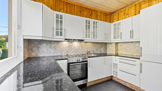 Praktisk hjørnekjøkken med laminat benkeplate og fliser over benk.