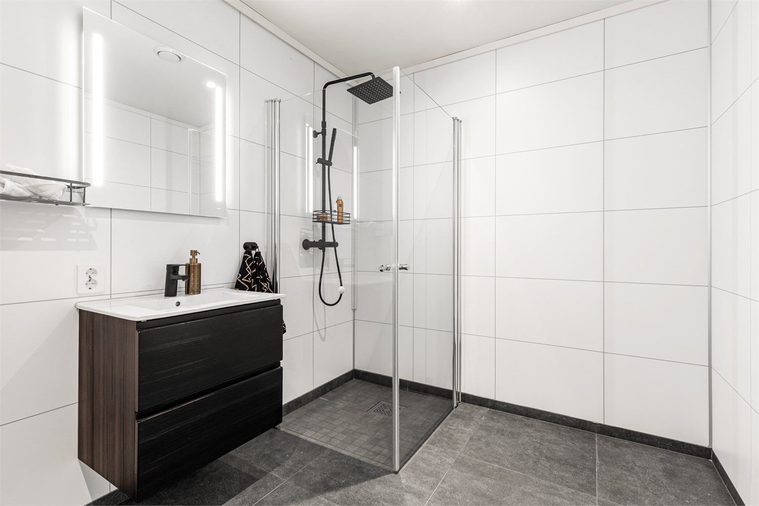 Vegghengt servantskap med ovenpåliggende servant og ett-greps armatur. Speil med integrert belysning over servant. Stikkontakt på vegg.