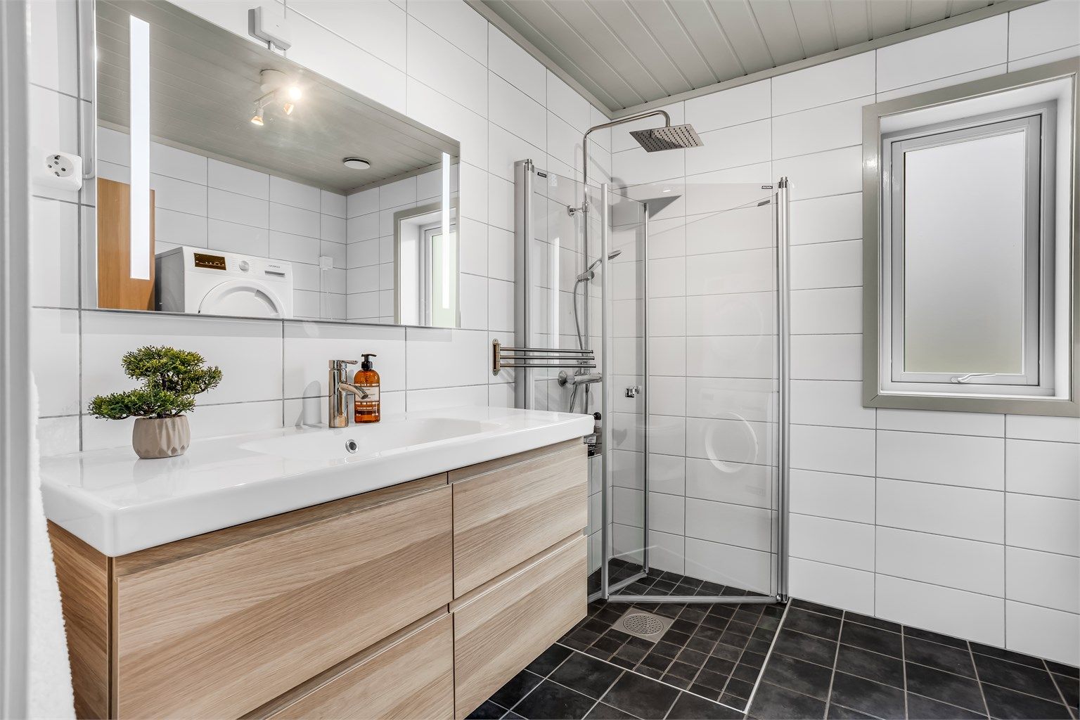 Badet i første etasje er bestående av blant annet: vegghengt servantinnredning med servant, speil med sidelys, vegghengt høyskap, dusjhjørne med glassdør og gulvstående toalett. 