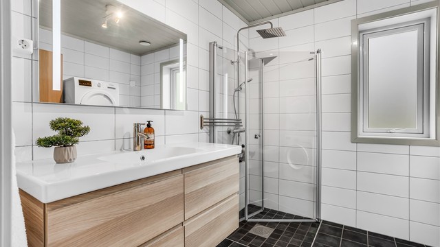 Badet i første etasje er bestående av blant annet: vegghengt servantinnredning med servant, speil med sidelys, vegghengt høyskap, dusjhjørne med glassdør og gulvstående toalett.