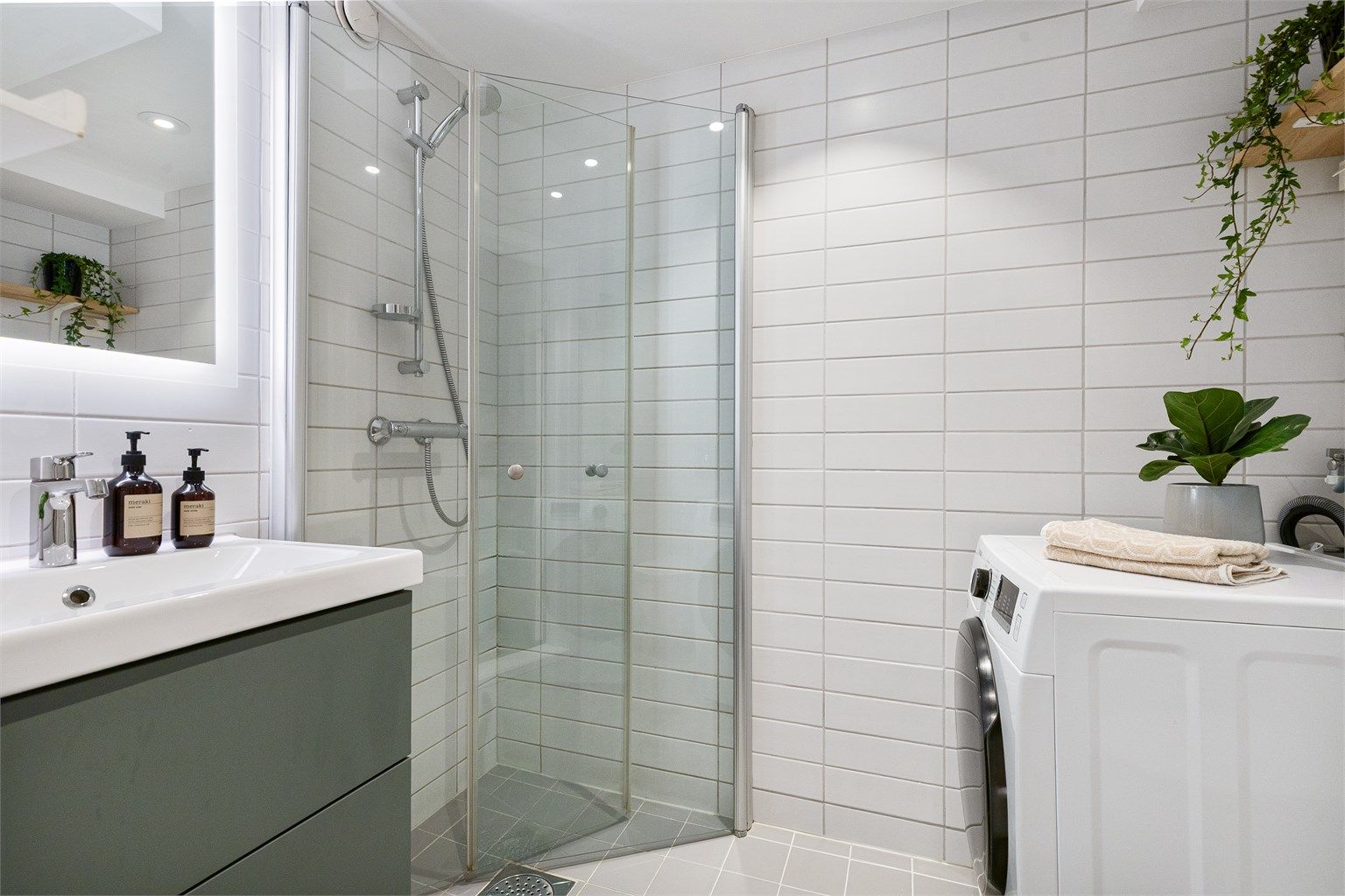 Badet har dusjnisje med glassdører og opplegg for vaskemaskin.