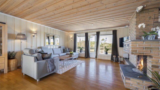 Romslig stue med god plass til en stor sofagruppe. Den sentralt plasserte peisen gir varme og en hyggelig atmosfære.