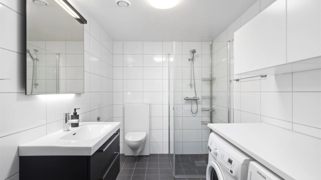 Innbydende og meget romslig bad med hvite fliser på vegg og grå fliser med varme i gulv