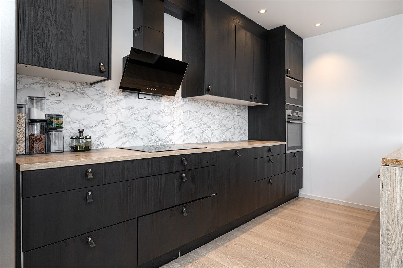 Moderne kjøkkeninnredning med mørke fronter, integrerte hvitevarer og rikelig med skap- og benkeplass.