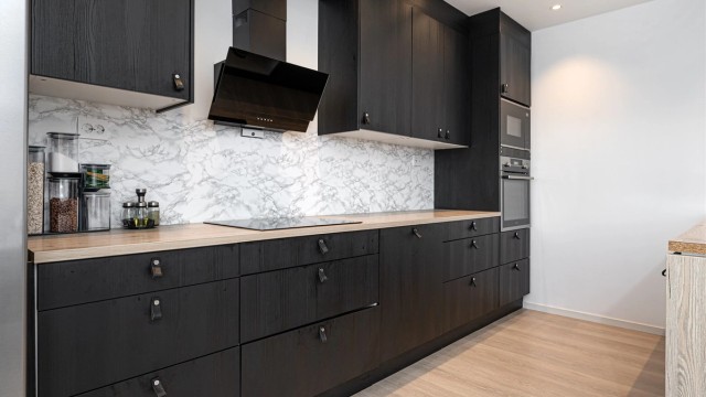 Moderne kjøkkeninnredning med mørke fronter, integrerte hvitevarer og rikelig med skap- og benkeplass.