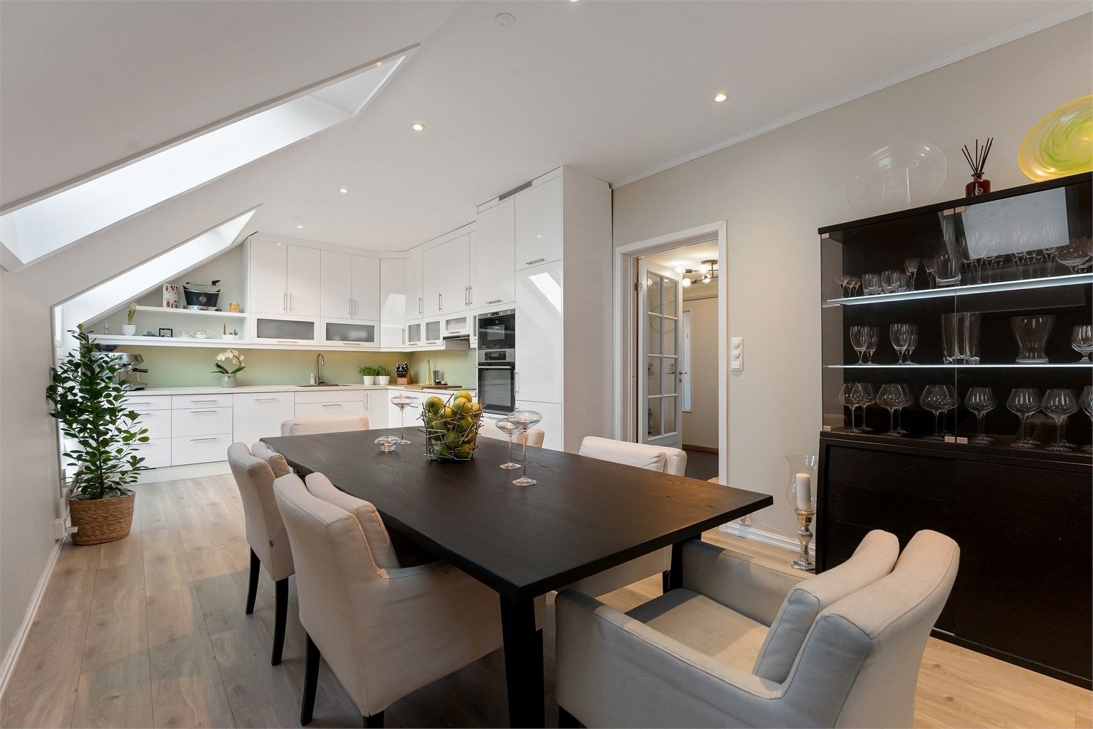 Hyggelig kjøkken med glatte fronter på skap og skuffer, benkeplater av tre med nedsenket oppvaskkum og glassplater mellom benkeplate og overskap