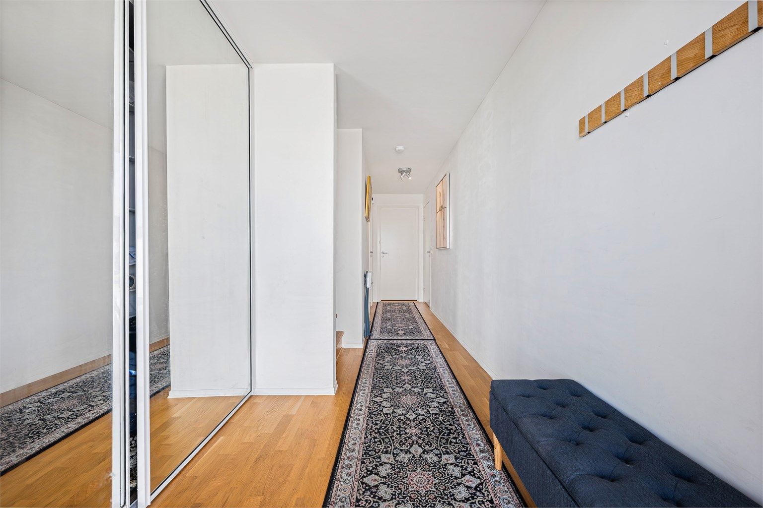 Entré med parkett på gulv, lyse vegger og romslig skyvedørsgarderobe med speilfronter.