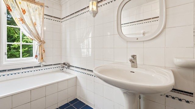Bad i første etasje, innredet med badekar og flislagte overflater.