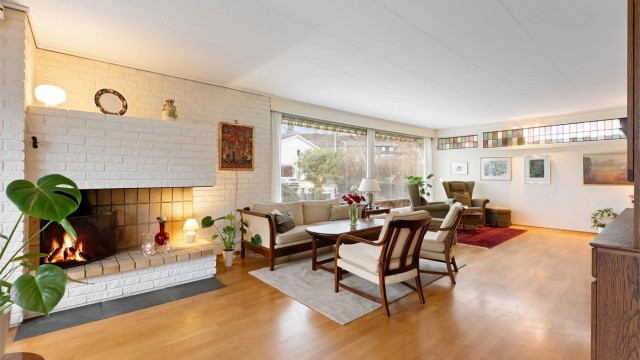 Den romslige stuen har parkett på gulvet og en sentral, åpen peis som et naturlig samlingspunkt.