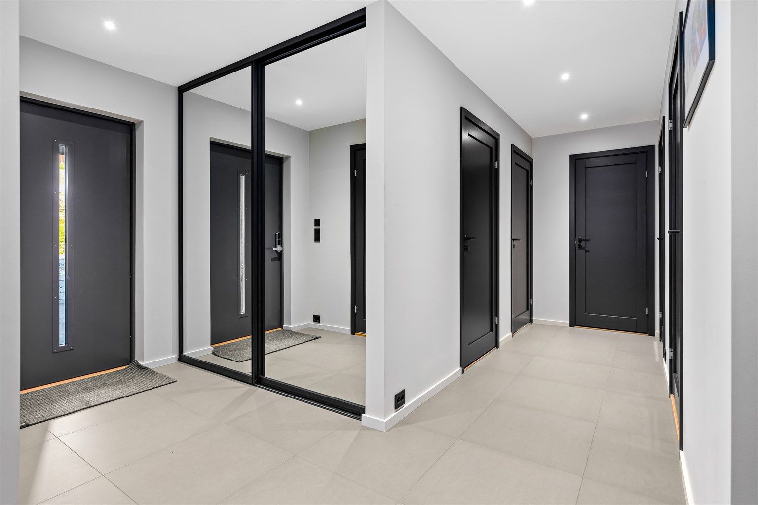 Fin gang med store fliser, varme i gulv og integrert garderobeskap med skyvedører.