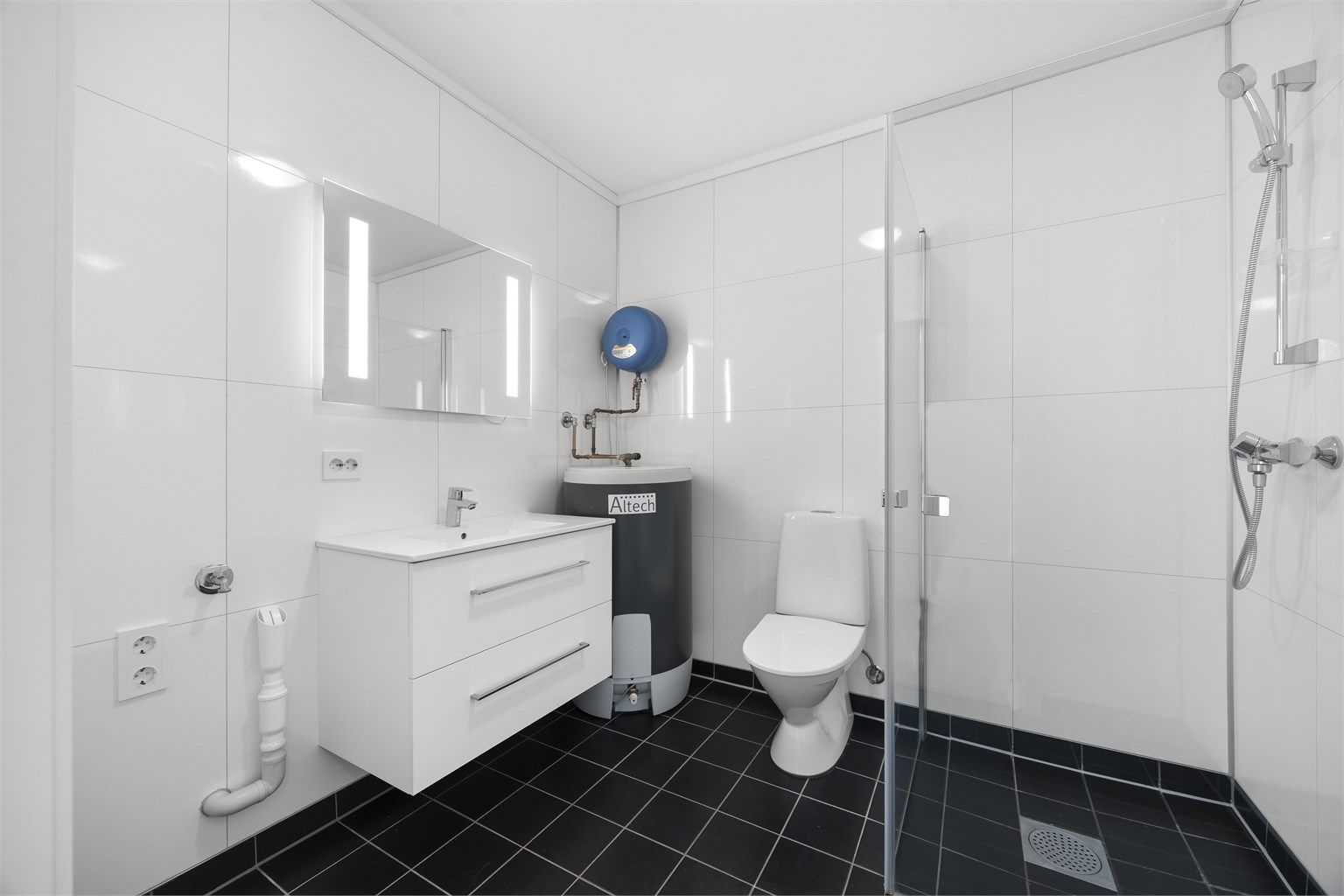 Badet har flislagt gulv med vannbåren varme, baderomsplater på vegg og opplegg for vaskemaskin.
