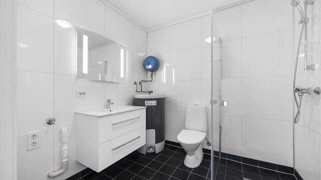 Badet har flislagt gulv med vannbåren varme, baderomsplater på vegg og opplegg for vaskemaskin.