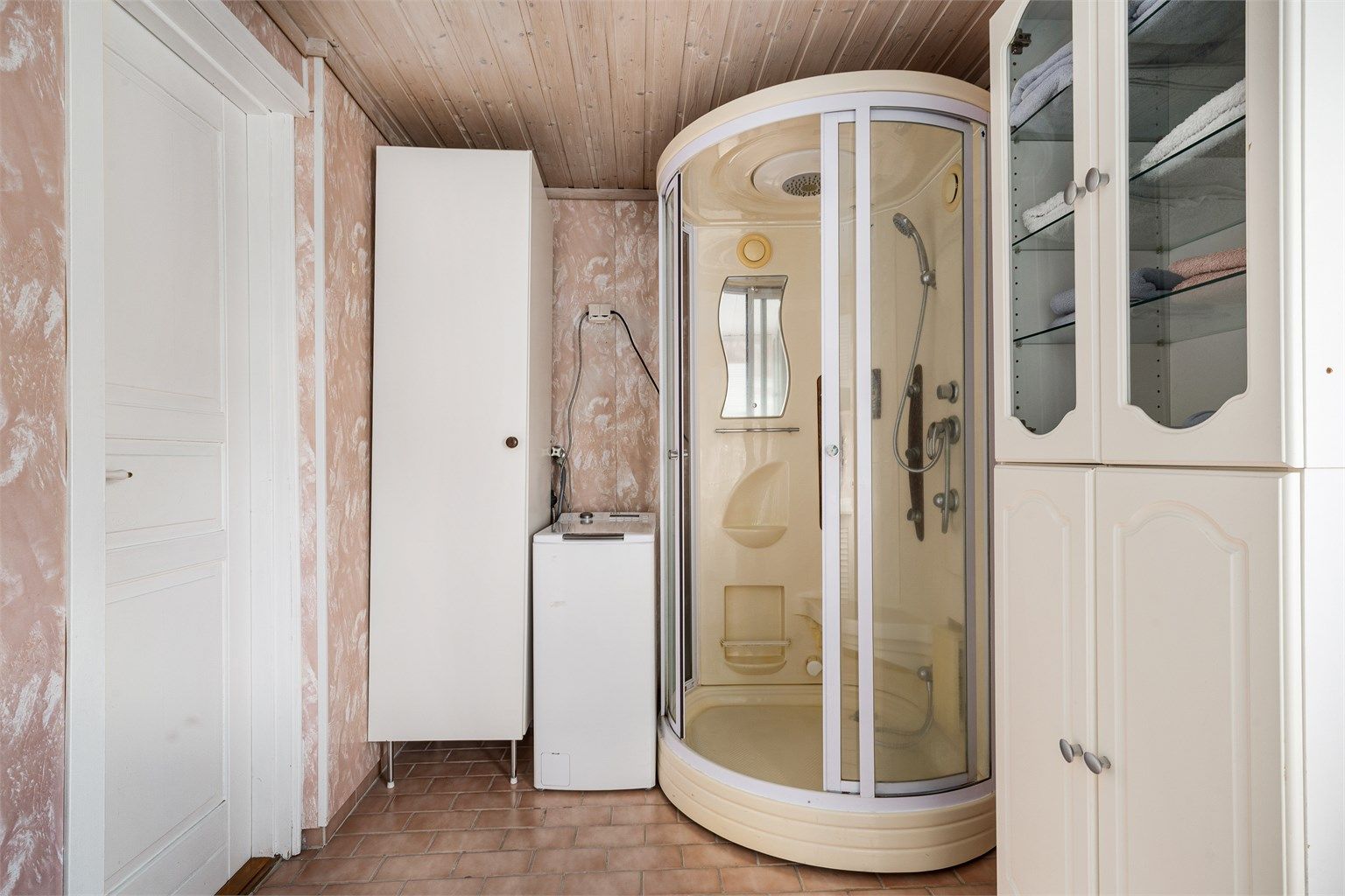 Badet med flislagt gulv og retro respatexplater på veggene er utstyrt med opplegg til vaskemaskin, dusjkabinett og servant i seksjon også den med retropreg.