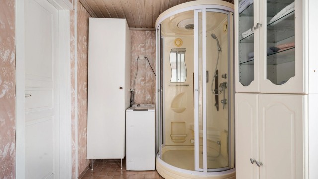 Badet med flislagt gulv og retro respatexplater på veggene er utstyrt med opplegg til vaskemaskin, dusjkabinett og servant i seksjon også den med retropreg.