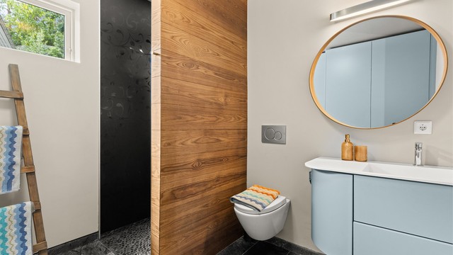 Badet er innredet med vegghengt toalett, servantinnredning med ovenpåliggende servant og speil med belysning. Praktisk dusjløsning gir et ryddig uttrykk.
