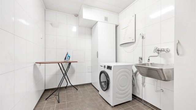 Separat vaskerom i kjelleren med flislagt gulv, utslagsvask og opplegg for vaskemaskin.