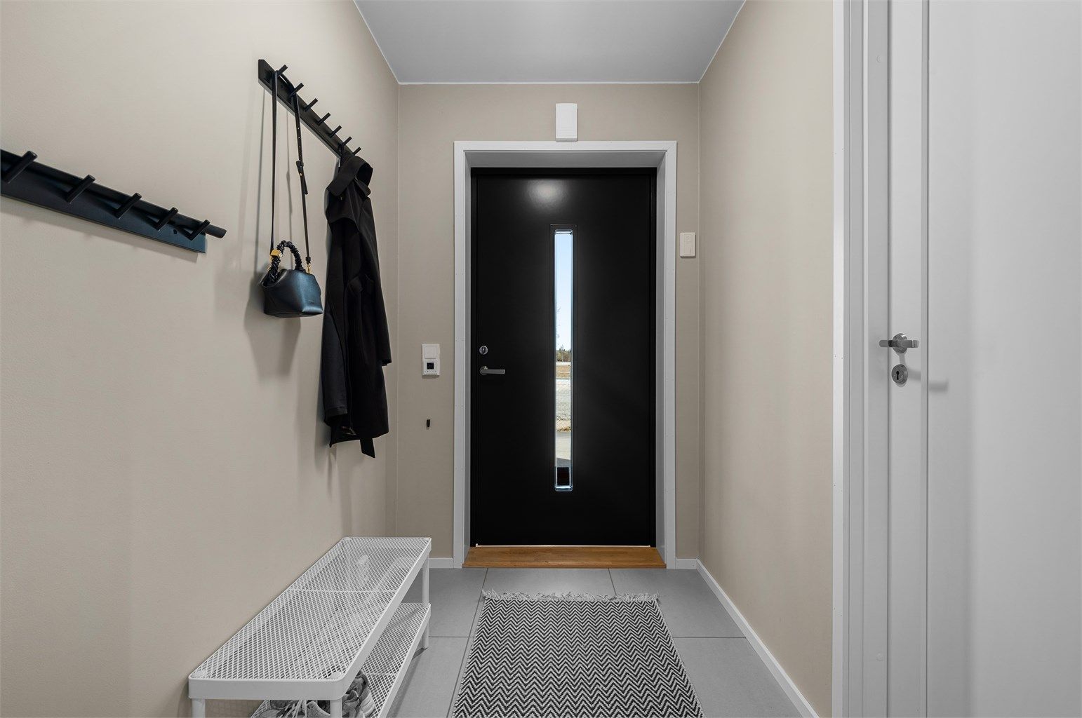 Ta av deg skoene og heng av deg jakken før du tar turen videre i ditt nye hjem. Fliser med varmekabler i gulv og oppheng for ytterklær på vegg. 