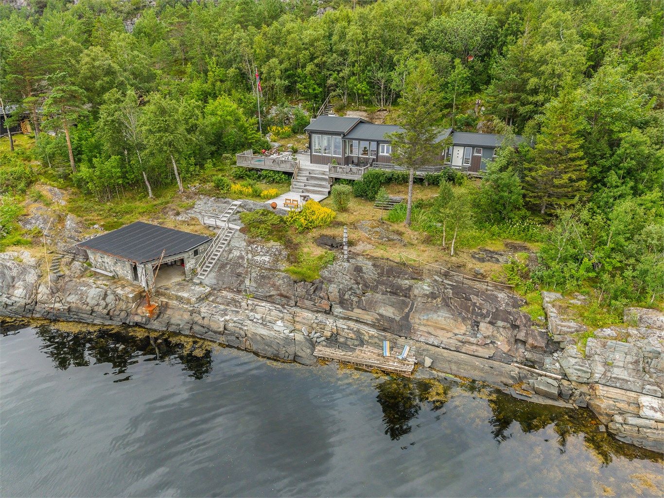 Dronebildet viser den flotte sammenhengen mellom hytta, de store terrassearealene, naustet og sjøen.