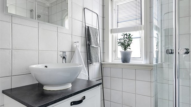 Innredet med servant på underskap og dusjhjørne med buede glassdører.