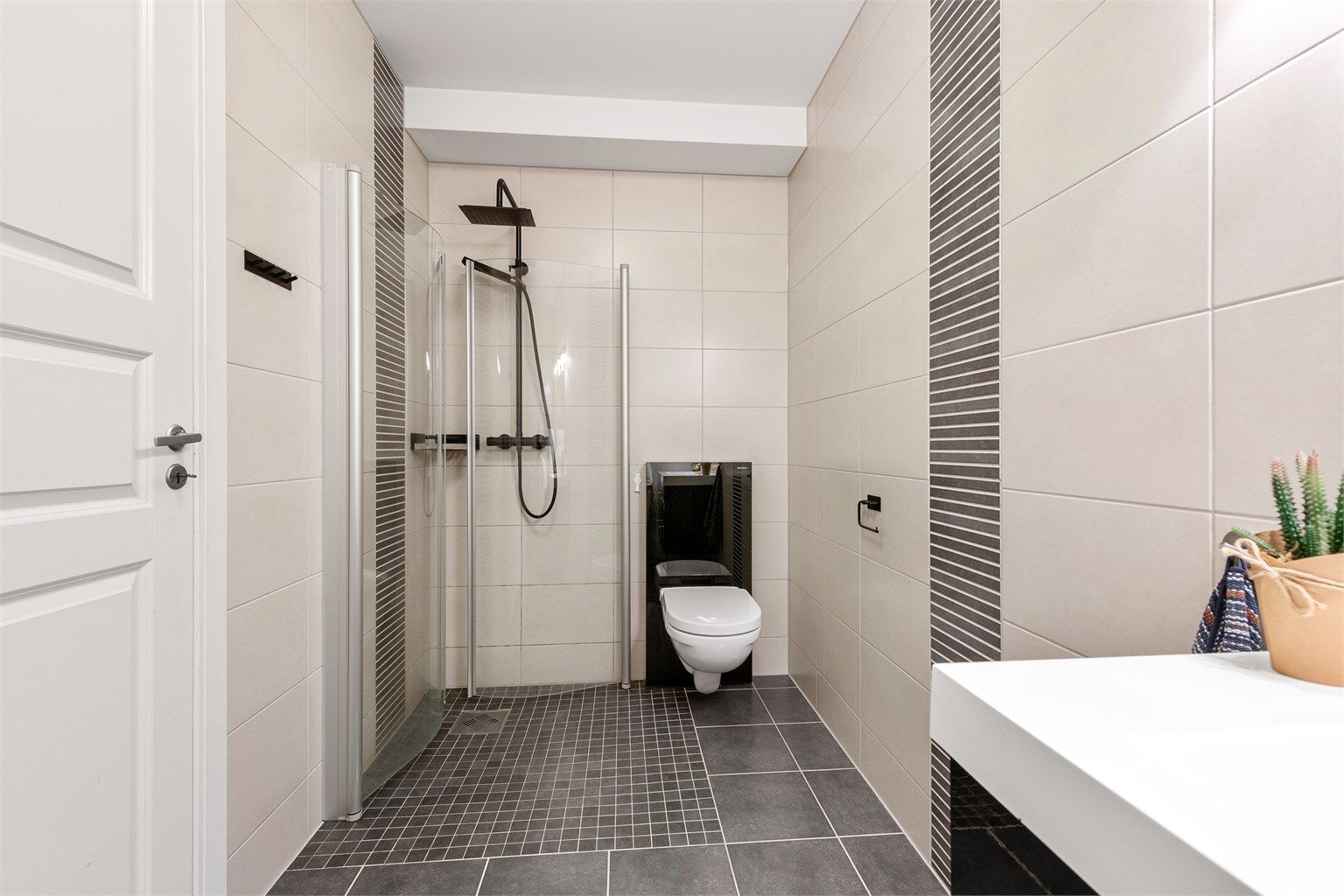 Dusjhjørne med foldbare glassvegger og vegghengt dusjarmatur på bad. Vegghengt toalett.