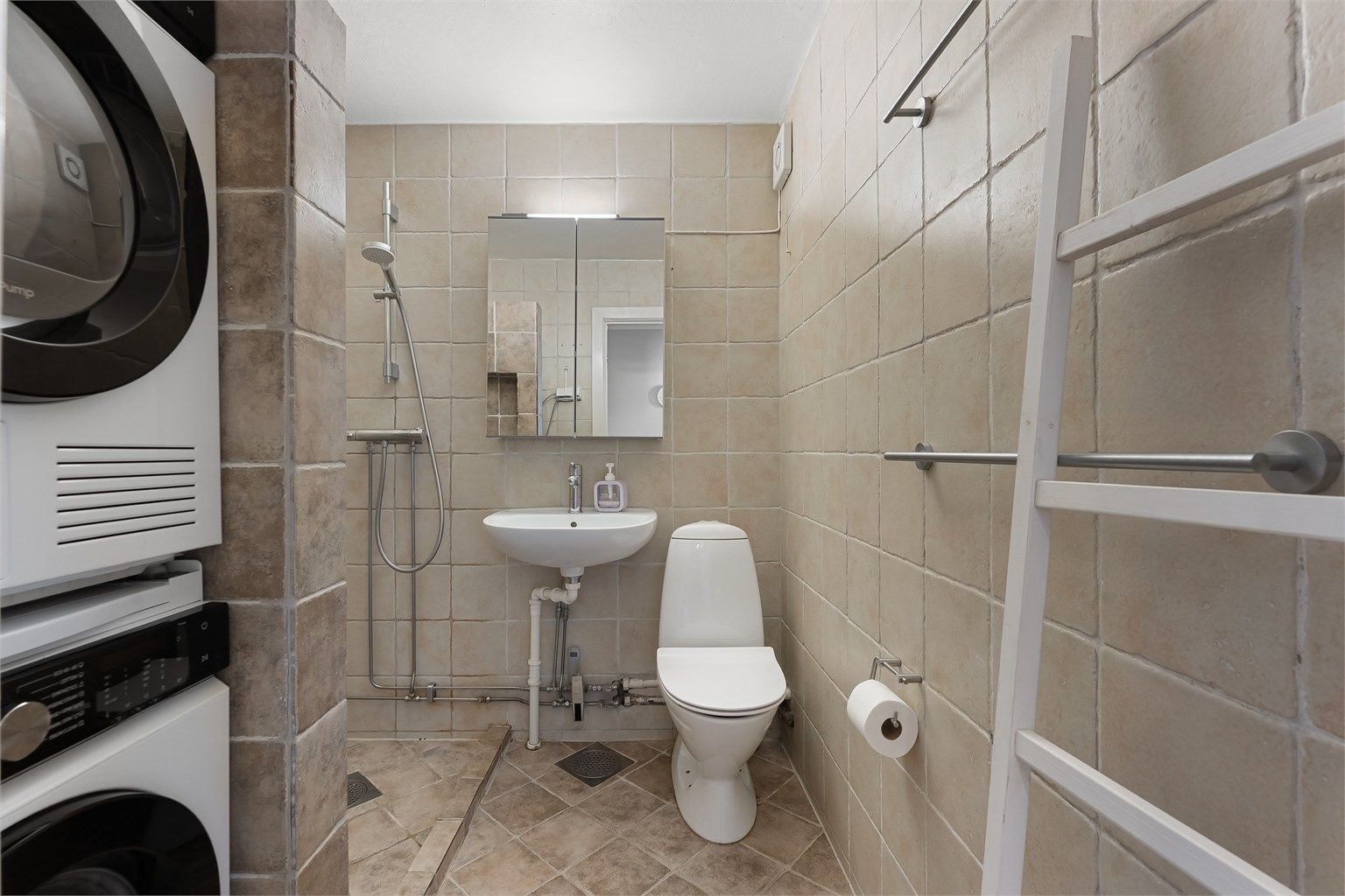 Flislagt bad med dusjhjørne og praktisk opplegg for vaskesøyle.