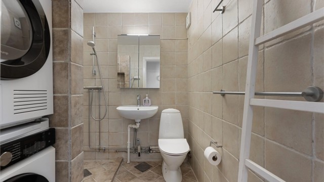 Flislagt bad med dusjhjørne og praktisk opplegg for vaskesøyle.