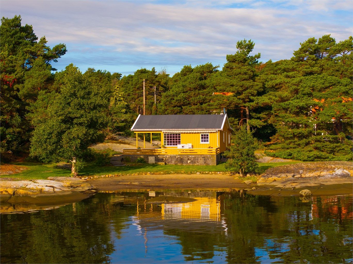 Helt nede ved vannkanten ved Skipstadsand på Asmaløy finner du denne gulmalte hytta, tilbaketrukket og ganske så usjenert.