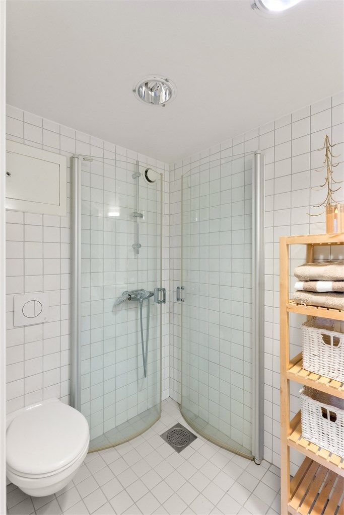 Badet er utstyrt med dusjhjørne med glassdører og vegghengt toalett.