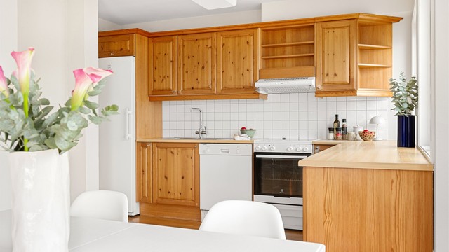 Åpen kjøkkenløsning med innredning fra byggeår. Profilerte fronter og benkeplate med laminert overflate.
Fliser mellom kjøkkenbenk og overskap.