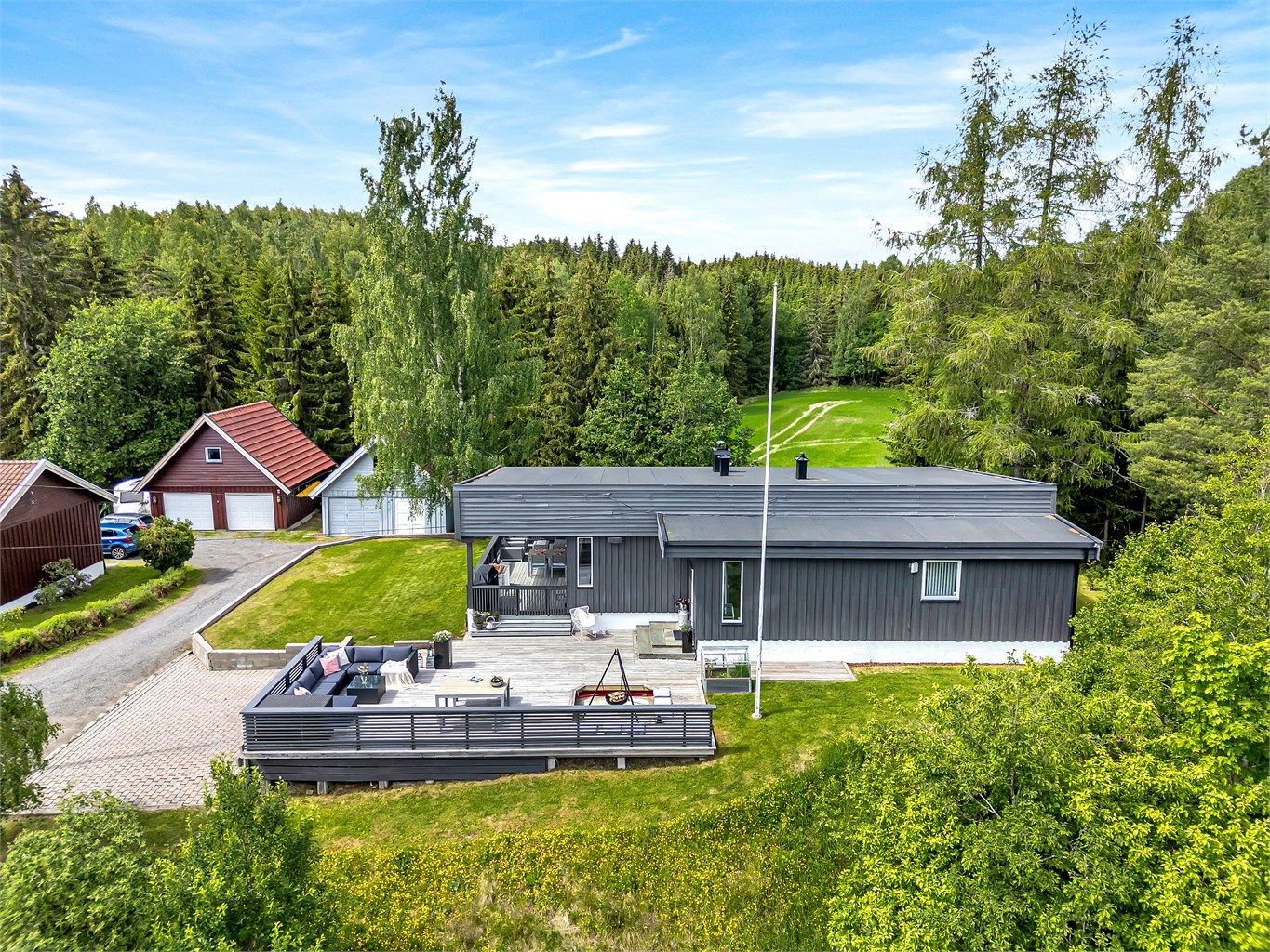 Gruset innkjøring inn til garasjen og belegningsstein på gårdsplass, som leder videre til boligens terrasse og inngangsparti.