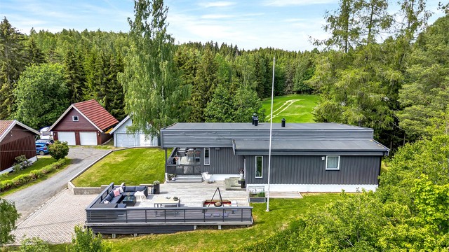 Gruset innkjøring inn til garasjen og belegningsstein på gårdsplass, som leder videre til boligens terrasse og inngangsparti.