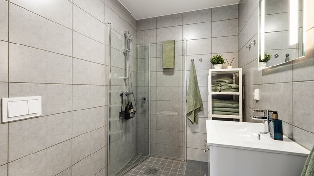 Bad i hovedetasjen med flislagt gulv med gulvvarme, vegghengt toalett og dusjhjørne med inn- og utadslående dører.