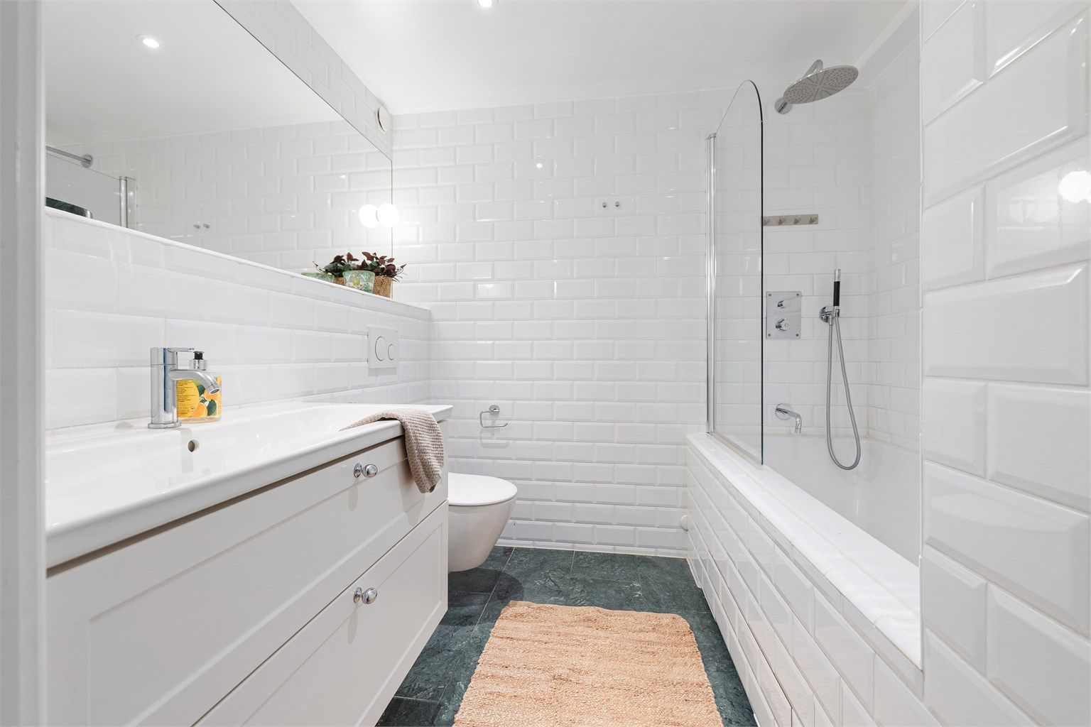 Baderommet er utstyrt med vegghengt servantinnredning med ovenpåliggende servant, vegghengt toalett og badekar med dusjløsning. Downlights i himling og mekanisk avtrekk gir god funksjonalitet og komfort.