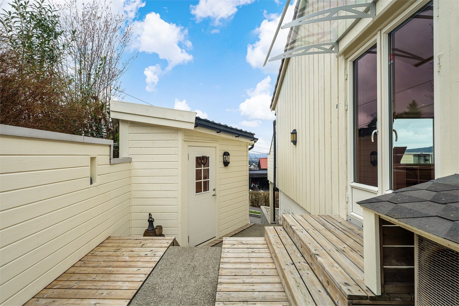 Fra stuen er det utgang til terrasse og gangvei til inngangsparti. Uthuset på bildet blir i dag brukt som kontor