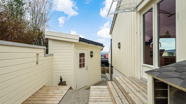 Fra stuen er det utgang til terrasse og gangvei til inngangsparti. Uthuset på bildet blir i dag brukt som kontor