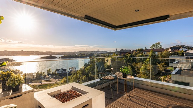 En lekker og overbygget altan med glassrekkverk og åpen gasspeis. Her har man full oversikt over skipsleden og fremgangen til det nye Sotrasambandet. Legg også merke til sol- og vindskjerming i himlings hjørnet.