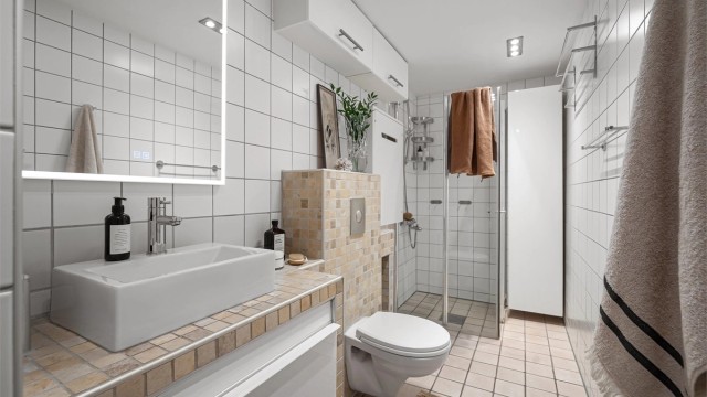 Badet er utstyrt med vegghengt toalett og dusjhjørne med innfellbare glassdører, hvorav én dør er leddet