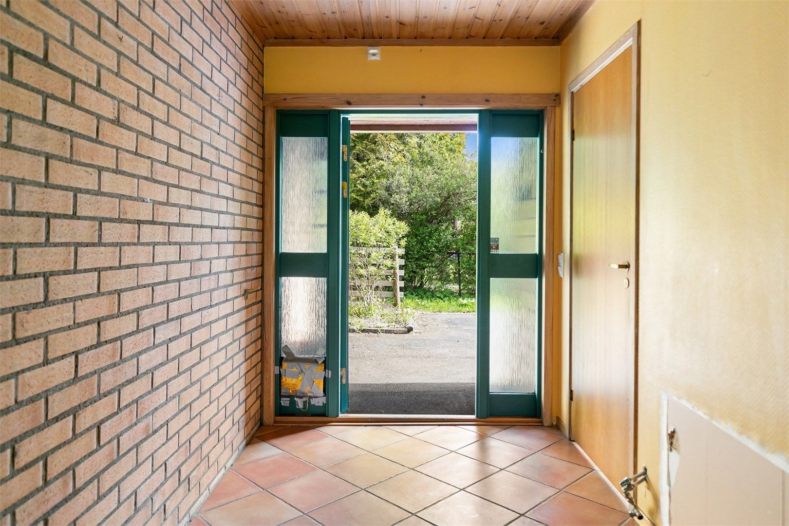 Entréen har flislagt gulv og en eksponert teglsteinsvegg som fortsetter inn i boligen.