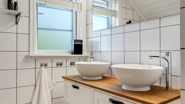 Baderomsinnredning med dobbel servant, benkeplate i treverk og speil med belysning.