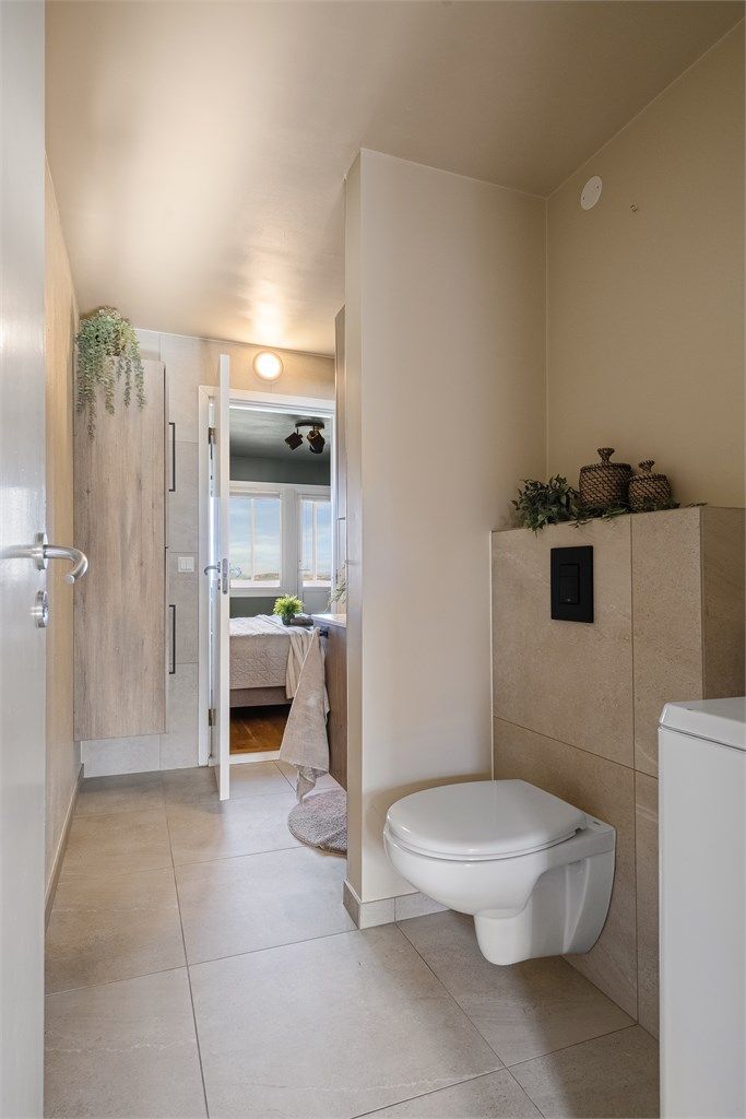 Vegghengt toalett og opplegg for vaskemaskin og plass til tørketrommel. Fine store fliser på gulv og i dusj, ellers malte vegger i lignende fargetone. 