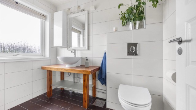 Baderommet har servantmontering på trebenk og vegghengt toalett.