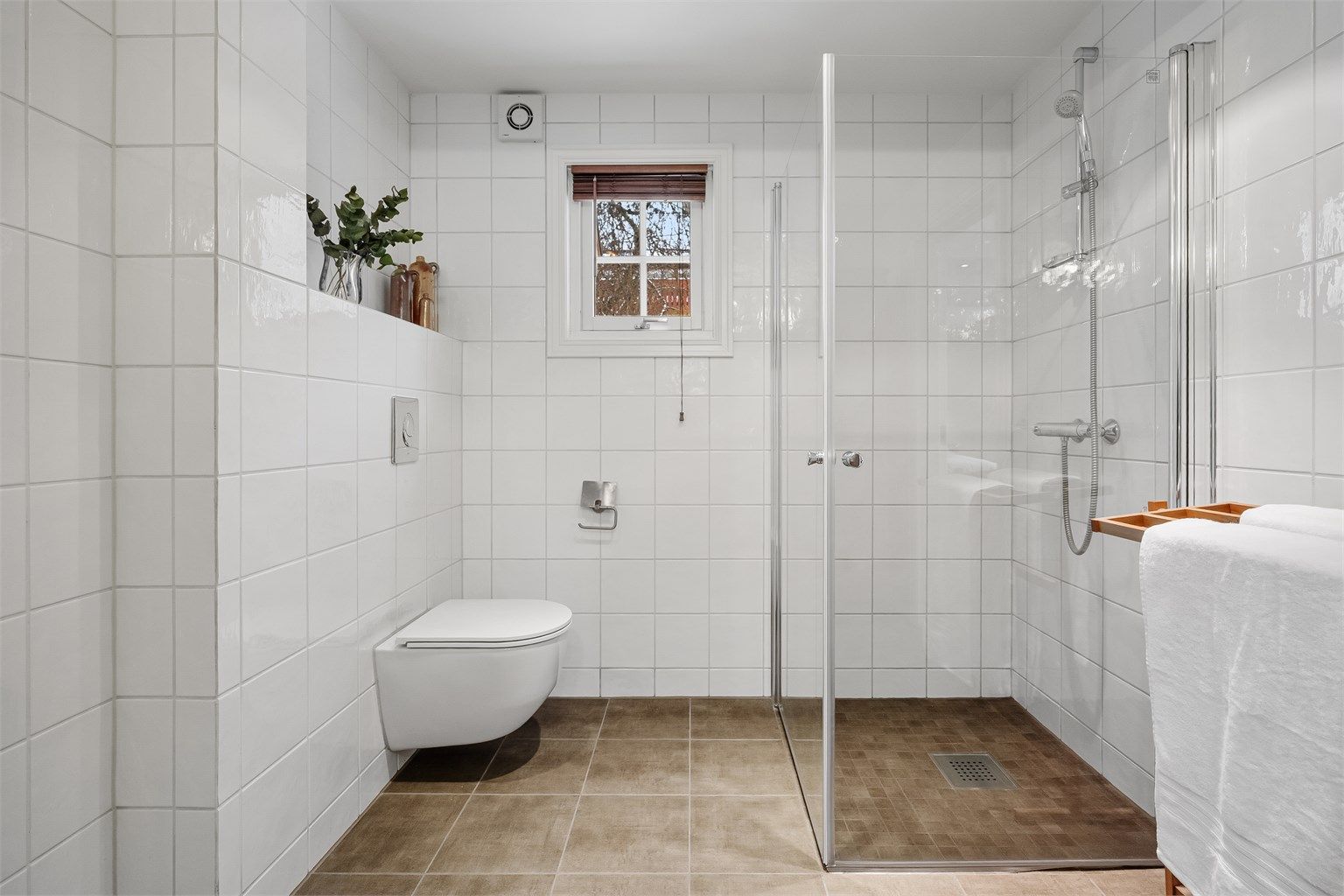 Rommet har et vegghengt toalett og et romslig dusjhjørne med svingbare glassdører.