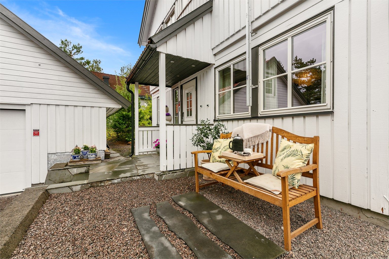 Et lunt og sjarmerende inngangsparti med sittebenk og grønne omgivelser.