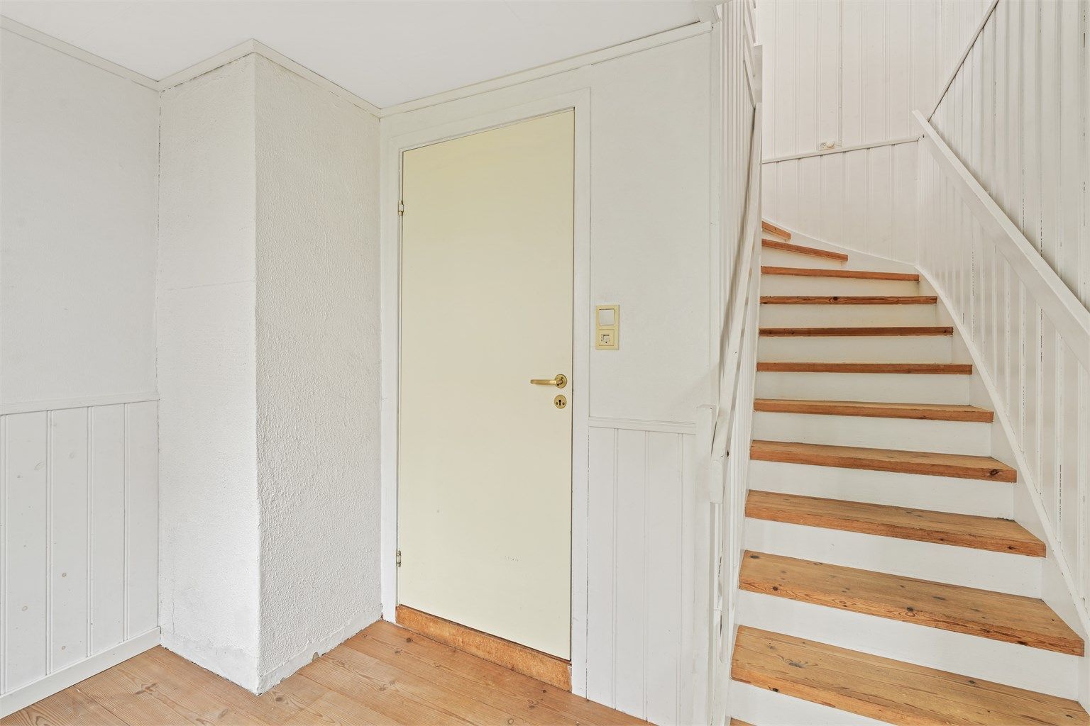 Hvitmalt tretrapp med lukkede trinn leder opp til andre etasje.