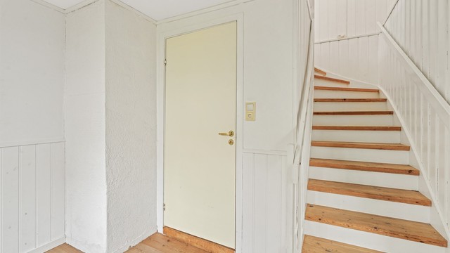 Hvitmalt tretrapp med lukkede trinn leder opp til andre etasje.