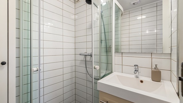 Servant i baderomsinnredning, speil og dusjhjørne med glassdører.