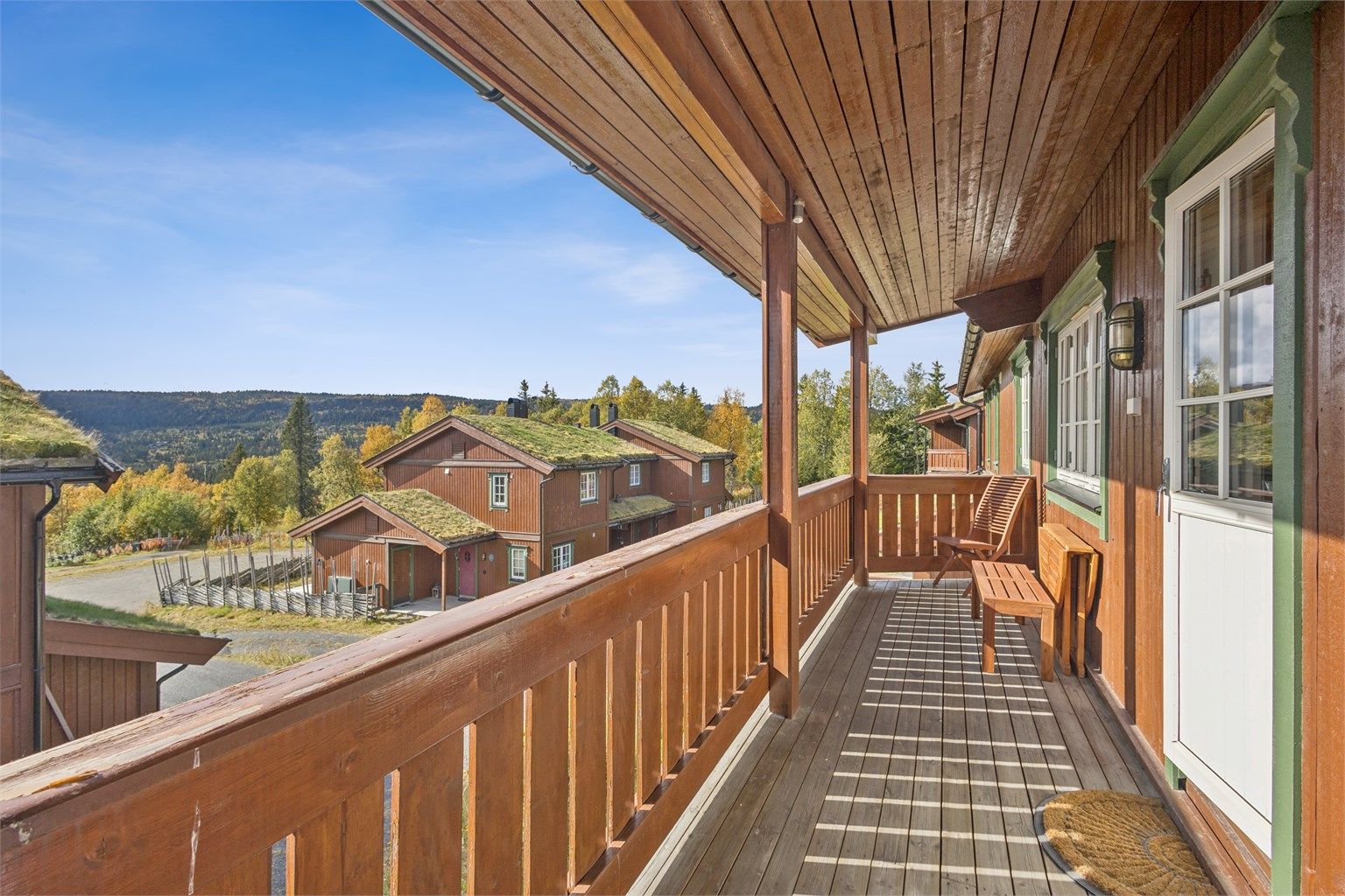 Overbygd balkong i trekonstruksjoner med terrassebord på gulv og utsyn over området.