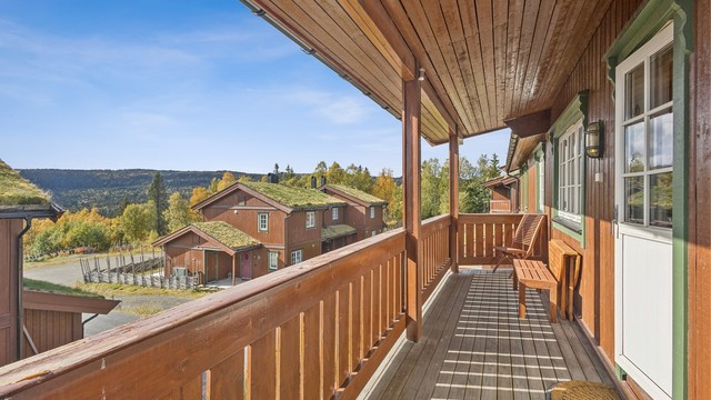 Overbygd balkong i trekonstruksjoner med terrassebord på gulv og utsyn over området.