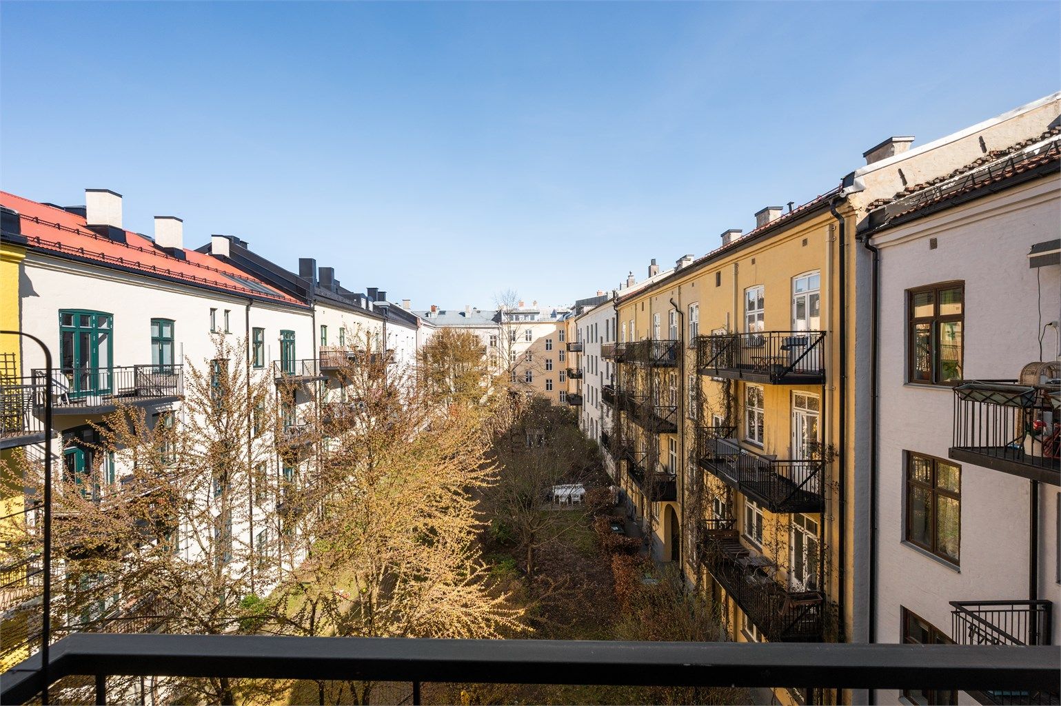 Utsikt fra balkongen mot den skjermede og grønne bakgården, et fellesareal som gir en rolig kontrast til det pulserende livet i Markveien.