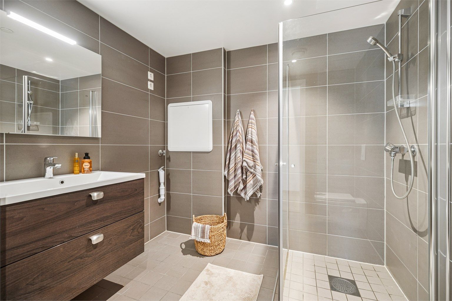 Lekkert flislagt bad med gulvvarme, vegghengt servantskap,  vegghengt toalett og dusjhjørne med glassdører. 